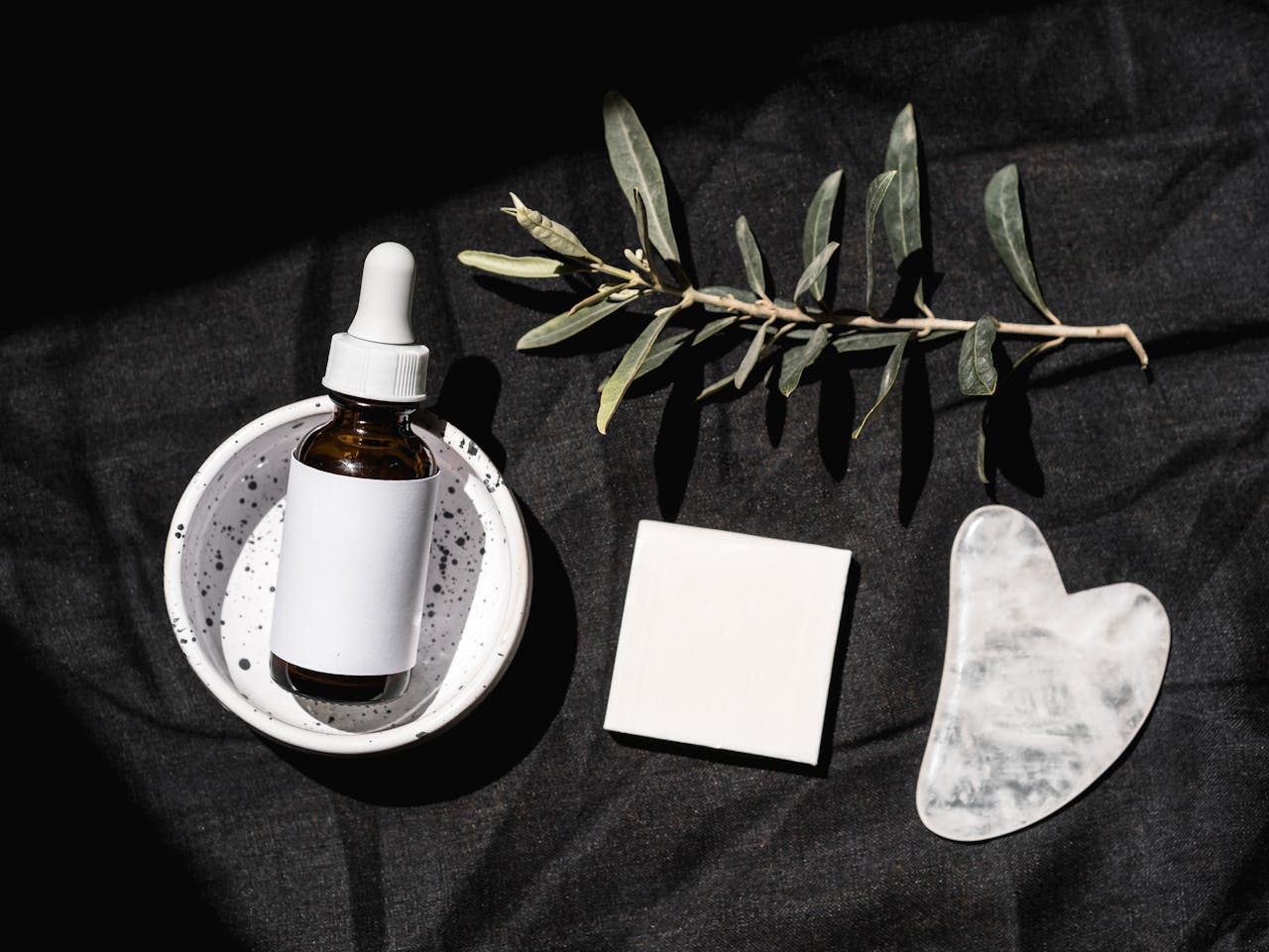 services-06 Elegant beauty product arrangement featuring a serum dropper bottle and gua sha on a black background.